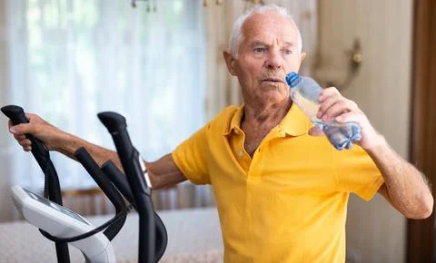 Senior man using elliptical trainer and drinking water Foto stock