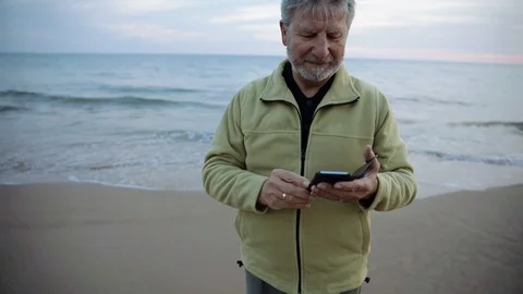Senior man using his phone next to the sea Stock Footage 103135930