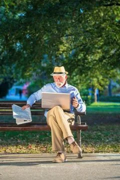 Senior man using laptop computer at rest in the park outdoors Stock Photos