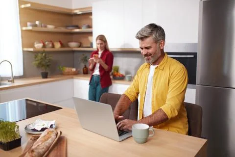 Senior Man Using Laptop At Kitchen. Happy Couple Spending Weekend Together Stock Photos