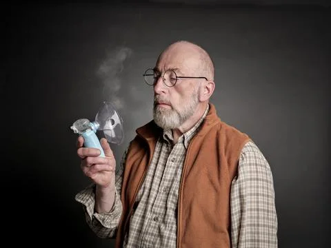 Senior man using a portable handheld nebulizer Stock Photos