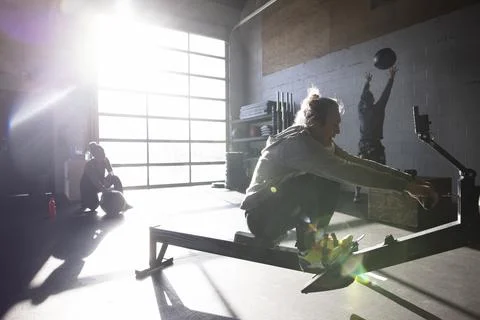 Senior man using rowing machine in sunny gym Stock Photos