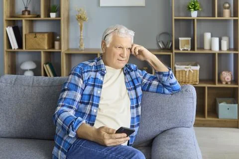 Senior man using smartphone on sofa at home, relaxing and reading messages Stock Photos