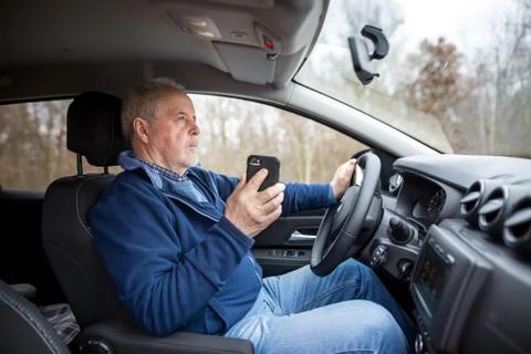Senior man using a smartphone while riding his new, modern car, transportation 库存照片