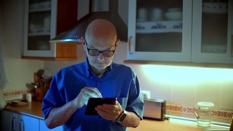 Senior Man Using Tablet in Kitchen at Night Under Blue Light Vidéo 337946112