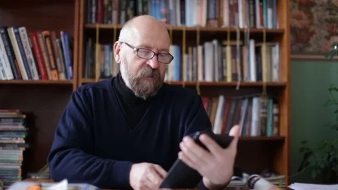 Senior man using tablet sitting on white couch in living room. Starting and Stock Footage 74735960