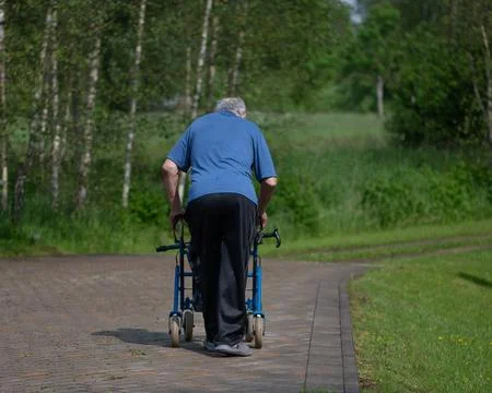 Senior Man Using Walker In Green Park Path Foto stock