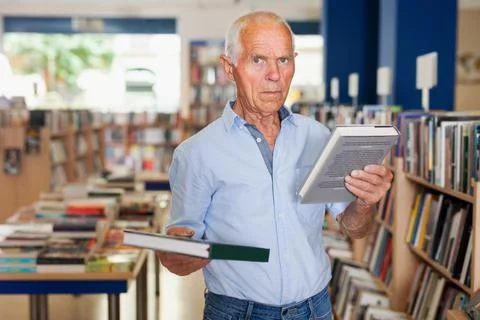 Senior man visitor looking for necessary literature on shelves Stock Photos