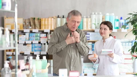 Senior man visits pharmacy and suffers from cough. Girl pharmacist offer help to Stock Footage 329394110