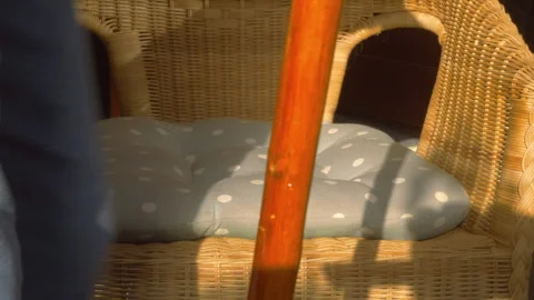 A senior man with a walking cane sitting down on a wicker chair. Stock Footage 255382292