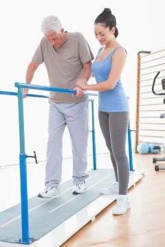 Senior man walking with parallel bars and coach help Stock Photos