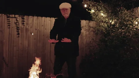 Senior man warming himself from a backyard firepit Stock Footage 221873778