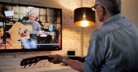 Senior man watching tutorial on internet television to play guitar hobby concept Vidéo 144683033