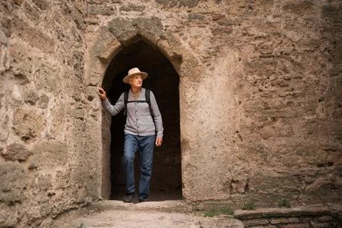 Senior man wearing hat with backpack on fortress wall arched window Stock Photos