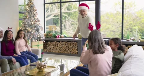 Senior man wearing Santa hat by Christmas tree selecting green gift, handing to Stock Footage 335453889