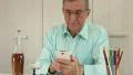Senior man with white mobile phone and bottle of cognac sits at a table HD Footage