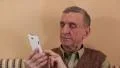 Senior man with white smartphone speaks, smiling and gesticulates HD Footage