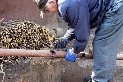Senior man in work gloves preparing a rusty metal pipe on a wooden stump lo.. Stock Photos