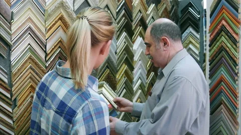 Senior man worker helping young female customer to pick up frame for a picture Stock Footage 123501554
