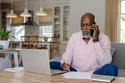 Senior man working from home, using laptop and talking on smartphone Stock Photos