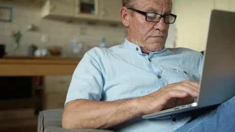 Senior man working on laptop computer sitting in his kitchen. Online banking Stock Footage 92367813
