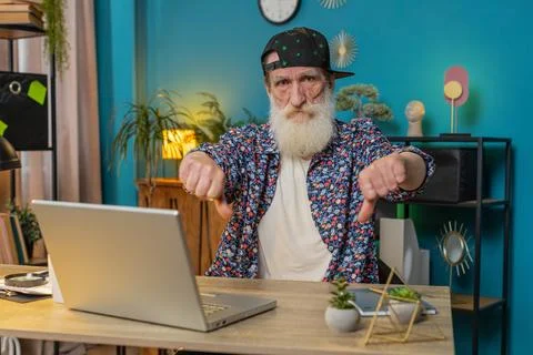 Senior man working on laptop computer at home office showing thumbs down sign Stock Photos