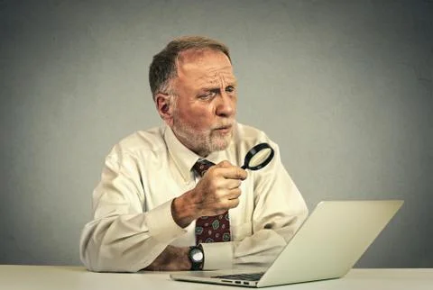 Senior man working looking through magnifying glass at laptop screen Stock Photos