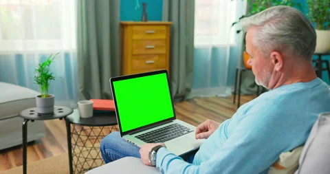 Senior Man Works on a Laptop Computer with Green Mock-up Screen Sitting on a Vídeo Stock 156298380