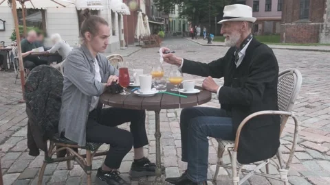 Senior man writes and clinks glasses with hipster in cafe Stock Footage 139796364