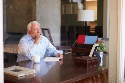 Senior man writing memoirs in book sitting at desk Stock Photos