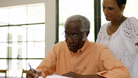 Senior man writing at a table as his wife looks over his shoulder Vidéo 88367929