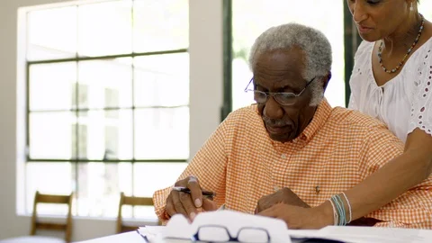 Senior man writing at a table as his wife looks over his shoulder Vidéo 88367939