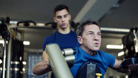 A senior man with a young trainer doing strength workout exercise in gym. 스톡 동영상 101734447