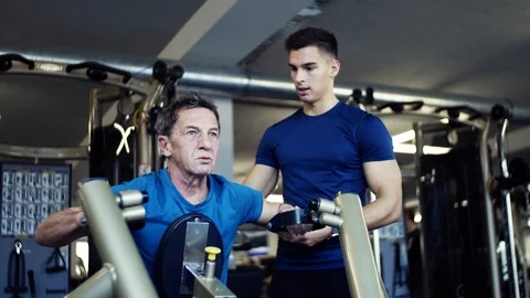 A senior man with a young trainer doing strength workout exercise in gym. Stock Footage 101974896