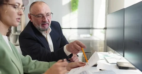 Senior manager mentoring analyst discussing financial report and data at desk Stock Footage 332717864