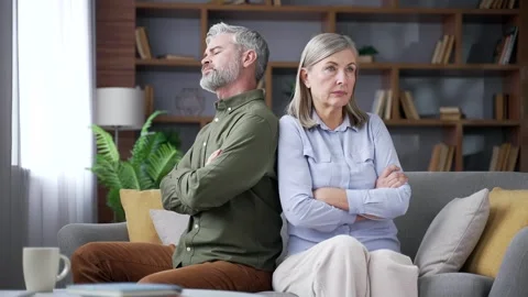 Senior married couple sitting on a sofa in the living room at home with crossed  Stock Footage 339775967