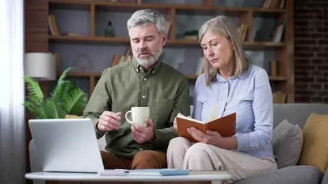 Senior married couple taking notes while watching an online webinar on a laptop  Stock Footage 339774511