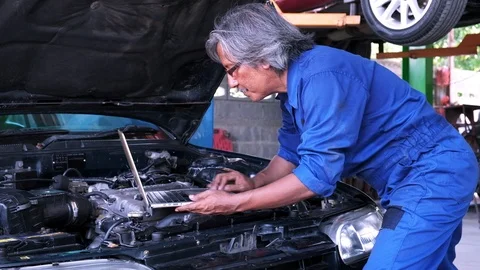 Senior mechanic checking engine of automobile with laptop computer in garage Stock Footage 119165418