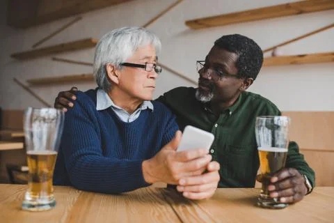 Senior men drinking beer while asian man showing smartphone to friend Stock Photos