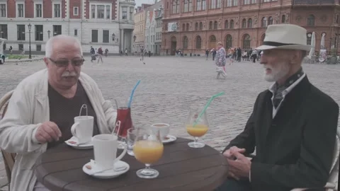 Senior men sit down on chairs at small table with drinks Stock Footage 139796157