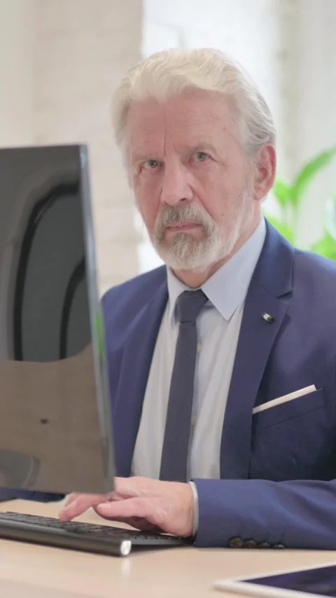 Senior Old Businessman Looking at Camera while Using Desktop Computer, vertical Stock Footage 328974373