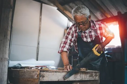 Senior old carpenter using saw working on wood craft at workshop to produce c Foto stock