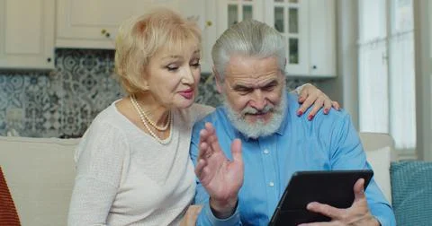 Senior old couple talking using digital tablet computer modern tech at home Foto stock