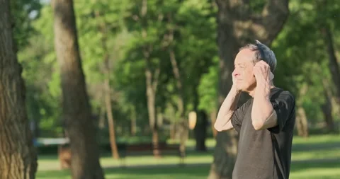 Senior old man puts on wireless headphones, start jogging in city park. Listen Stockbeeldmateriaal 244384265