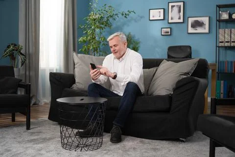 Senior old man talking using cell phone computer modern tech at home on weekend Foto stock
