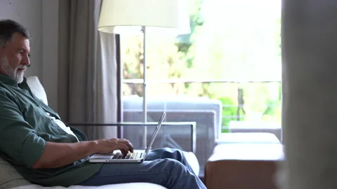 Senior old mature man typing on laptop browsing internet using apps sit on sofa Stock Footage 158836341
