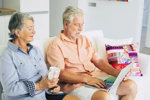 Senior old people couple at home sit down on the sofa use laptop computer and Stock Photos