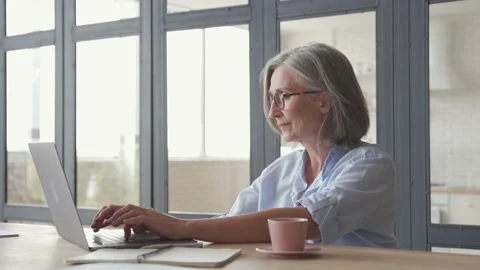 Senior older middle aged woman using laptop computer sitting at workplace. Stock Footage