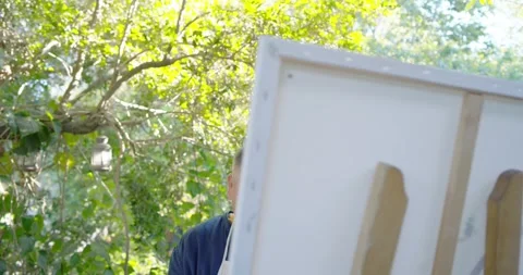 Senior painter stepping behind canvas in apron taking phone pics checking shots Stock Footage 340012153