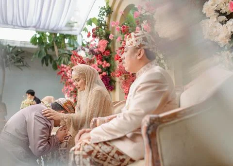 Senior parent sitting on a couch while their groom and bride kiss their han.. Stock Photos